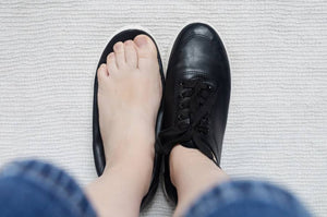 Top-down view of a bare foot beside a black shoe, illustrating fit and the need for supportive footwear.