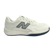 Side view of a New Balance men's court shoe. Suitable for tennis, pickleball and netball. Has a white mesh upper with a black sole.