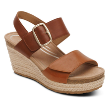 A women's wedge espadrille sandal featuring tan leather velcro straps with a gold-tone buckle, a braided jute wedge heel, and a cork midsole.