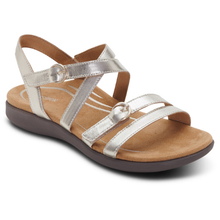 A single women's strappy sandal in metallic champagne leather with gold-tone buckle details covering a hook and loop fastening and a dark brown sole.