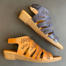 Two women's cutout wedge sandals shown on a dark gray background, one in navy blue and one in tan/caramel brown leather.