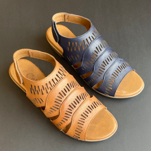 Two women's cutout wedge sandals shown on a dark gray background, one in navy blue and one in tan/caramel brown leather