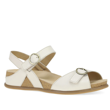 An ivory white leather sandal with adjustable ankle and instep straps, featuring gold-tone metal buckles, a cork midsole, and a brown outsole.