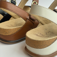 Close-up of a pair of wedge sandals showing the tan leather straps, cork-wrapped wedge heels, and beige insoles on a white background.