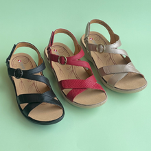 Three women's strappy wedge sandals arranged on a mint green background. The sandals feature black, red, and taupe/beige straps with a textured pattern on the center strap, and a circular buckle closure.