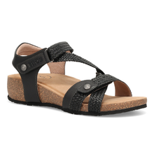 The Taos Trulie, a single women's flat sandal with black straps, woven detailing, and a natural cork wedge heel and footbed.