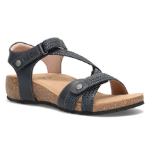 The Taos Trulie, a single women's flat sandal with dark navy blue straps, woven detailing, and a natural cork wedge heel and footbed.