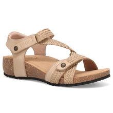 The Taos Trulie, a single women's flat sandal with beige straps, woven detailing, and a natural cork wedge heel and footbed.